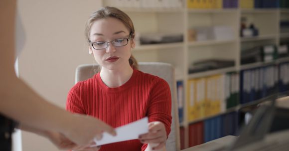 Accountant - Serious young female employee in casual clothes and eyeglasses reading attentively document while working in office with colleague