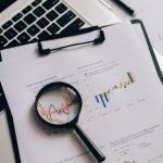 Stock Market - Magnifying Glass on White Paper with Statistical Data
