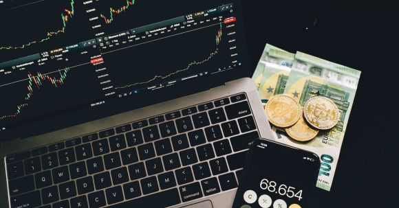 Stock Market - Bitcoins and Paper Money Beside a Cellphone and Laptop with Graphs on Screen